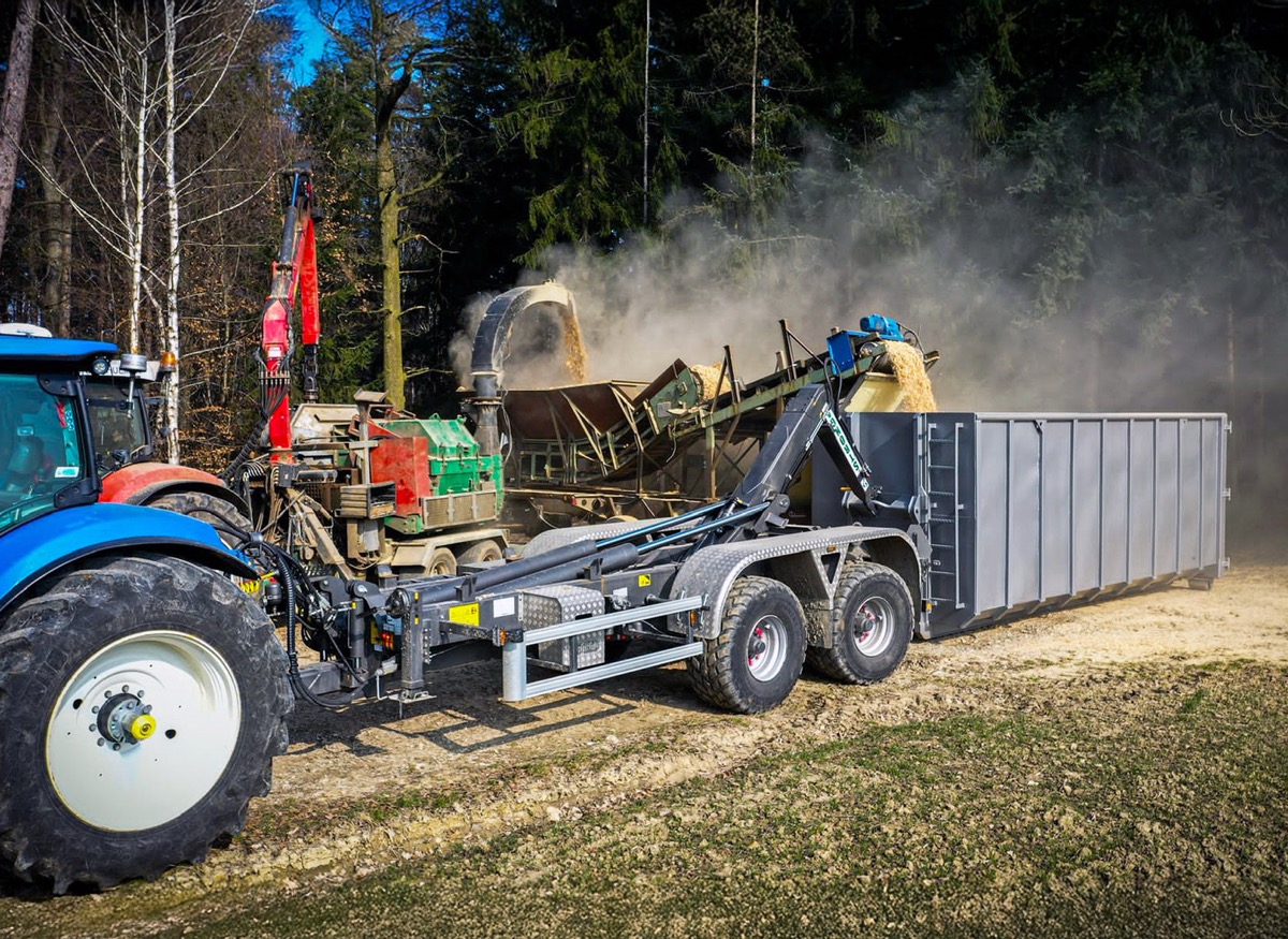 Grünes Holz wird in einen am Boden abgestellten Container mithilfe eines Stronga-Abrollkippers gehäckselt, bereit zur Anlieferung an die Strömungstrocknungsanlage